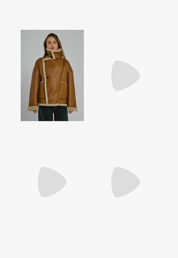 Donna che indossa una giacca in pelle foderata in shearling color sabbia con chiusura asimmetrica e colletto alto, in piedi di fronte a uno sfondo grigio uniforme.; Maglione corto a maniche corte nero in maglia con scollo rotondo e orlo a costine. Tessuto liscio con vestibilità comoda. Design minimalista.; Jeans flare in denim blu scuro con leggeri sbiadimenti, vita standard e un classico design a cinque tasche. Accenti in hardware color rame.; Stivale Chelsea in suede beige con pannello laterale elastico nero, suola nera spessa e linguetta alla caviglia.; Borsa in pelle blu dalla forma arrotondata, con una sola tracolla, chiusura con zip e nome del marchio in rilievo sulla parte anteriore. Texture liscia.