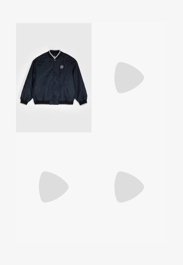 Converse RETRO CHUCK VARSITY JACKET - Bomberjacks - black; Witte katoenen t-shirt met ronde hals, korte mouwen en een klein zwart "W.W." logo op de linkerborst. Gladde textuur, reguliere pasvorm.; Bruine katoenen utility broeken met een rechte pijpdesign, voorzien van voorzakken en metalen hardware accenten voor extra duurzaamheid.; Zwarte hoge sneakers met witte zool en veters, gecombineerd met losse blauwe denim jeans, rustend op een grijze leuning.
