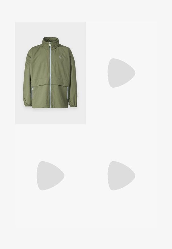 Giacca verde oliva con colletto alto, cintura frontale, polsini elasticizzati e due tasche laterali; presenta un piccolo logo sul petto.; T-shirt a maniche lunghe nera in cotone, con scollatura rotonda e un piccolo logo di coccodrillo ricamato in verde sul lato sinistro del petto.; Jeans di denim azzurro chiaro con una vestibilità ampia, gambe dritte, design a cinque tasche e chiusura con bottone in vita. Dettagli di cucitura minimalista.; Sneaker Lacoste grigie scure in materiale mesh e sintetico, con suola testurizzata e dettagli marroni sul colletto e sul branding.