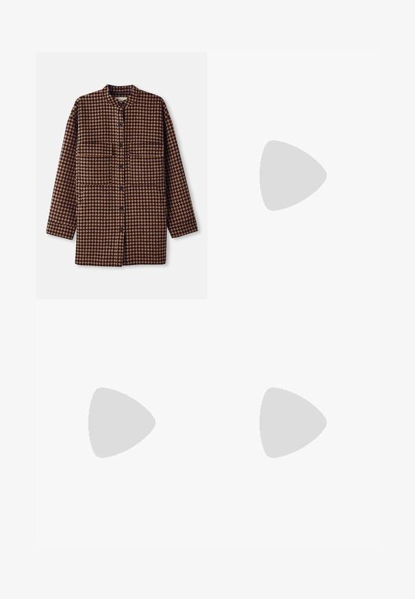 Giacca camicia in motivo houndstooth marrone e nero, con colletto alla cinese, chiusura frontale a bottoni e due tasche sul petto.; Maglietta nera a maniche corte con collo rotondo e un'etichetta bianca all'interno del colletto con la scritta "D.R.C. EST. 2002" su sfondo bianco.; Jeans blu a gamba larga in denim con vita alta, tasche frontali e cuciture a contrasto. Il tessuto ha una consistenza liscia.; Stivale alla caviglia in suede marrone con pannelli elastici laterali, punta arrotondata e una spessa suola in gomma con un motivo di battistrada testurizzato.