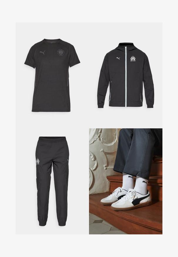 Giacca leggera nera con cappuccio, caratterizzata da una zip frontale, logo Puma bianco e design di Marsiglia sul petto, polsini elasticizzati e tasche laterali.; Maglietta sportiva nera a maniche corte con colletto rotondo, caratterizzata da una sottile trama orizzontale e un logo circolare del club sul petto.; Pantaloni sportivi neri realizzati in tessuto leggero. Presentano una vita elastica, tasche laterali e loghi grigi su ciascun lato.; Sneakers Puma in suede bianco e nero, con suola in gomma marrone. Abbinati a calzini bianchi con logo nero, indossati con pantaloni scuri.