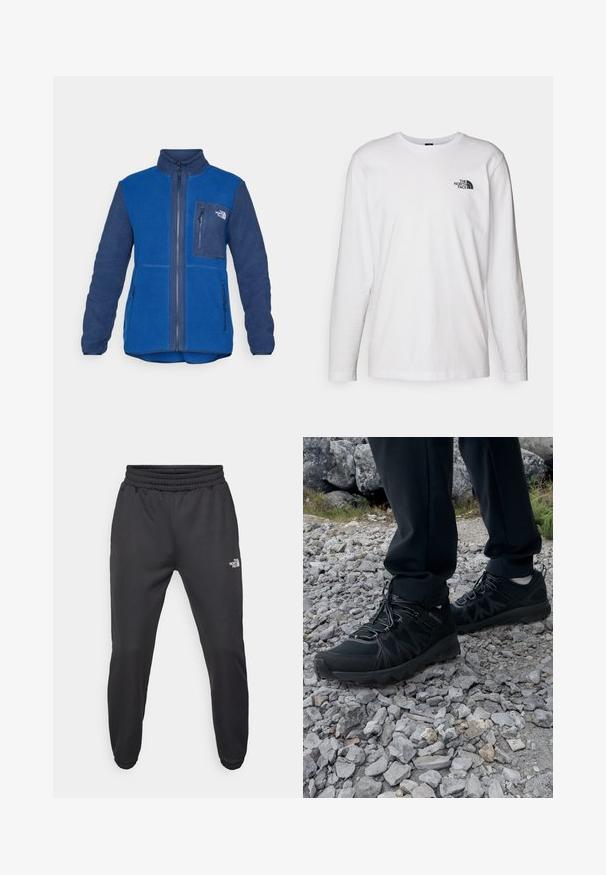 Niebieska polarowa kurtka z zamkiem z przodu, stójką, kieszenią na piersi i dwiema kieszeniami bocznymi. Posiada kontrastujące granatowe rękawy oraz różnice w fakturze.; Biała koszulka z długim rękawem wykonana z bawełny, z okrągłym dekoltem. Posiada małe czarne logo na piersi. Gładka faktura, regularny krój.; Czarne dresy z elastycznym paskiem w talii, zwężanym krojem, elastycznymi mankietami i małym białym logo na lewej udzie, wykonane z gładkiego materiału.; Czarne buty outdoorowe wykonane z siateczki i materiału syntetycznego, z fakturowaną cholewką, zabezpieczonym systemem sznurowania i solidną podeszwą, na skalistym terenie.