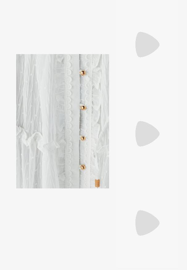 Hvid kjole med tekstureret stof, flæser, cirkulær blondekant og guldtonede knapper. Subtil prikmønster forbedrer designet.; Hvide kilehæle med en vævet espadrille-sål, der har en glat overdel og en subtil metallisk detalje ved hælen. Grå stribede bukser er synlige.; Cremefarvet, blødt kunstlædertaske med sammenkrøllede detaljer, justerbar rem og diskret snørelukning. Glat overflade og afrundet form.; Guld hoop øreringe med tre hvide perler, der fremviser en glat tekstur og en rund form, med en lille guld accent under perlerne.