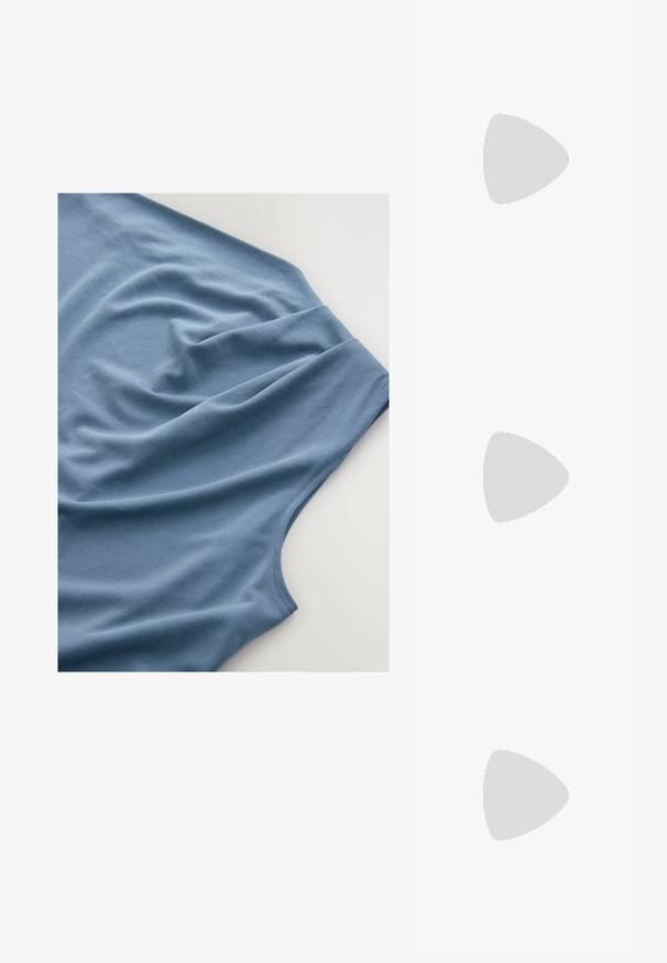 Camiseta azul vista desde arriba, con una tela suave de textura lisa, pliegues drapeados y un escote redondeado.; Zapato de tacón bajo en ante marrón con puntera afilada y tachuelas redondas plateadas en la parte superior y los lados, sobre un fondo blanco liso.; Bolso de mano metálico dorado con un diseño estructurado, textura suave y correa ajustable. Presenta una forma triangular única y un cosido minimalista.; Pendientes en tono dorado que presentan formas texturizadas y onduladas. Incluyen aros de clip esculturales y un diseño de aro abierto con un acabado martillado.