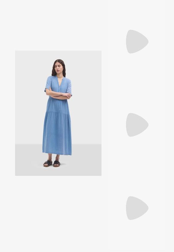 Vestido azul claro, hasta la rodilla, hecho de una tela suave. Presenta mangas cortas, un cierre de botones y una sección inferior fluida y fruncida.; Zapatillas de cuero blancas, diseño de corte bajo, con una textura suave, puntera redonda, cordones en la parte delantera y un pequeño logo bordado en el lateral.; Bolso negro de cuero en forma de media luna con un acento de hardware dorado, con cierre de cremallera. Llevado cruzado sobre un suéter gris.; Pendientes de botón en tono dorado con un diseño retorcido. Cada pendiente cuenta con un respaldo circular transparente para una sujeción segura.