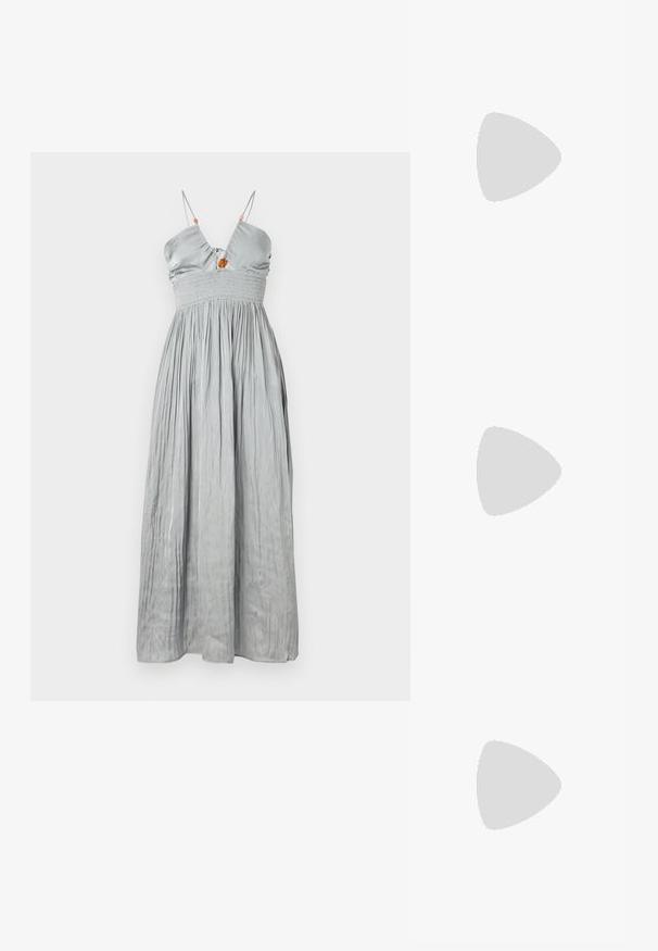 Mouwloze grijze satijnen jurk met een aansluitende bodice en een smocktail. Kenmerkt zich door dunne bandjes en een geplooide rok met een decoratief centrumdetail.; Zwarte gepolijste leren enkellaars met een spitse neus en een blokhak van gemiddelde hoogte. Glad textuur en minimalistisch ontwerp.; Zwarte handtas met gestructureerde vorm, gladde textuur en een metalen sluiting. Gecombineerd met brede zwarte broeken en sandalen met open teen op een houten vloer.; Gouden creolen met een getextureerd ontwerp en drie heldere kristalaccenten aan één zijde, wat een moderne geometrische esthetiek biedt.