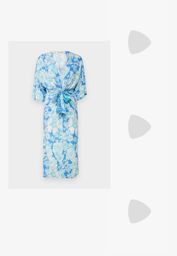 Diane von Furstenberg LIZA DRESS - Obleka iz džersija - blue; Črne usnjene sandale s peto, ki imajo priponko za gleženj. Imajo gladko teksturo, odprt prst in tanek peto. Podrobnost z zlatim sponko.; Bela usnjena torbica z teksturirano površino, ki vključuje zlat pas in črne detajle. Ima sprednji žep in zadrgo.; Kovrjanje rjave lase, svetla polt, nosi zlat uhani. Ozadje je nevtralno sivo, kar omogoča osredotočanje na lastnosti obraza subjekta.
