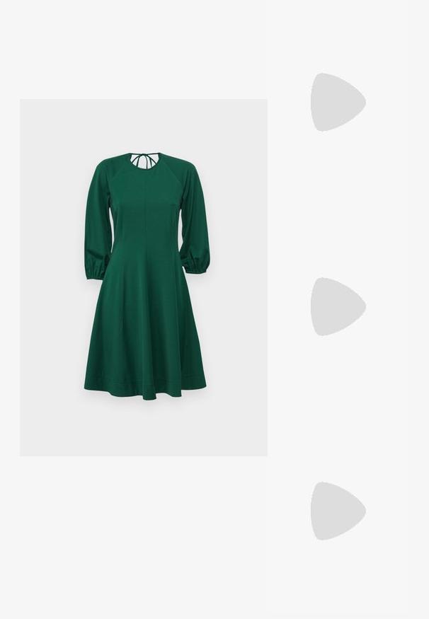 Robe verte avec de longues manches bouffantes, encolure arrondie et corsage ajusté. Fabriquée en tissu doux, elle s'évase doucement à la taille jusqu'à l'ourlet.; Baskets en cuir blanc, design bas, avec une texture lisse, bout rond, lacets à l'avant et un petit logo brodé sur le côté.; Sac demi-lune en cuir noir avec des accents en métal doré, doté d'une fermeture éclair. Porté en bandoulière sur un pull gris.; Boucles d'oreilles avec clou en métal doré et design torsadé. Chaque boucle d'oreille est dotée d'un arrière transparent circulaire pour un port sécurisé.