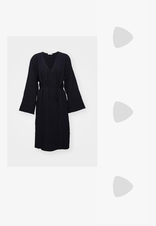 Sort tekstureret omslagskjorte med lange brede ærmer og et tyndt taljebånd, knælængde på en helt hvid baggrund.; Hvide slingback hæle med spids tå, der har en glat overdel, subtile udskæringer og en lav blokhæl. Den sorte sål fremhæver designet.; Sort læder tote taske med to lange stropper, en indsnøret top og et gyldent cirkulært accent. Glat tekstur med et minimalistisk design.; Dramatiske dråbeøreringe med fire rektangulære klare krystaller indsat i sølvfarvet metal. Hver krystal har en facetteret overflade for ekstra glans.