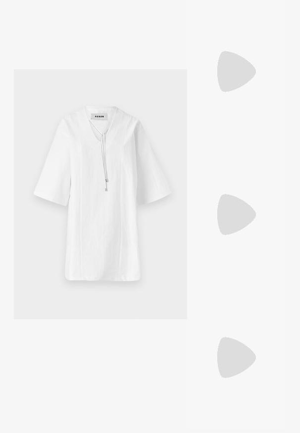 Valkoinen pellavapaita, jossa on V-pääntie ja lyhyet hihat. Ripustettu nauha kaulassa ja tikatut yksityiskohdat vartalon varrella.; Tumman viininpunainen patentoitu nahkaloaferi, jossa on teksturoitu pinta, matala lohkare-Korko ja klassinen pennin nauhakuva, kuvattuna sivulta.; Mustan nahkatote-bag, jossa on kaksi pitkää kantohihnaa, nyöri ylhäällä ja kultainen pyöreä koriste. Silkkinen pinta ja minimalistinen muotoilu.; Koralliileveys kultasävyiset metallikorvakorut, joissa on veistoksellinen, spiraalimainen muotoilu. Ominaisuuksiin kuuluu sileät pinnat ja valoa heijastavat kaaret.