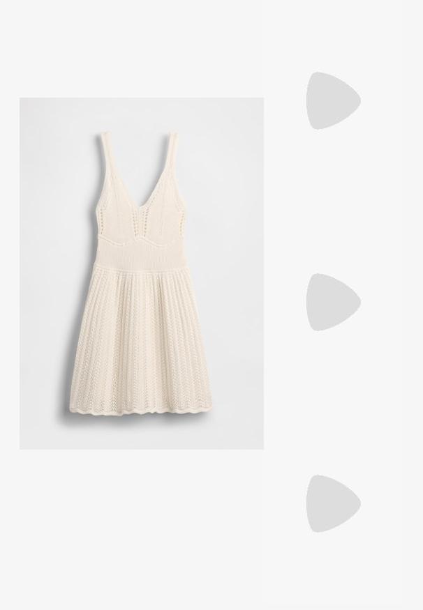 Stickad klänning i krämfärg med V-ringning, ribbad överdel och utsvängd kjol med vågig fåll och hålmönster över hela plagget.; Beige spetstoppad slingback-sko med svart kant, guldspänne och en kraftig blockklack på grått golv med mörkgrön bakgrund.; Vit syntetisk handväska med triangulär form, platt framklaff och rosettdetalj, justerbar rem, slät textur och minimalistisk design.; Örhängen i guldton med texturerade, vågiga former. Inkluderar skulpturala clip-on-stift och öppen hoop-design med hamrad finish.