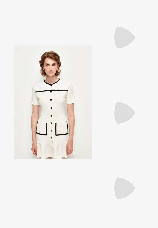 Cremefarbenes Kleid mit kurzen Ärmeln, runder Halslinie, schwarzen Akzenten, vorderem Knopfverschluss und zwei aufgesetzten Taschen. Ausgestellter Saum.; Blassrosa Slingback-Ballerinas mit spitzem Punkt, aus einem glatten, lederähnlichen Material. Mit Ausschnitten an den Seiten und einem flachen Absatz.; Beige Leder Crossbody-Tasche mit einer Schleifendetail, goldenen Beschlägen und einem verstellbaren Tragegurt, getragen über einer grünen Steppjacke.; Sechser-Set aus goldenen Ringen mit unterschiedlichen Designs: einer mit einer einzelnen Perle, ein weiterer mit mehreren kleinen Perlen und verschiedenen Texturen.