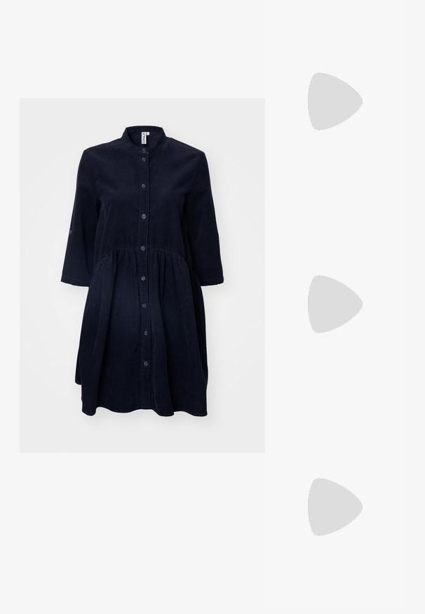 Mornarsko modra kordurovarna obleka z gumbi spredaj, ovratnikom mandarin, rokavi do tri četrtine in nabranim pasom. Mehka tekstura in dolžina do kolen.; Črne lakirane slingback pete s koničastim nosom in geometrijsko blokasto peto. Imajo eleganten, minimalističen dizajn in gladko teksturo.; Črna usnjena torbica s ukrivljeno obliko, z odstranljivo naramnico in zlatimi dodatki. Torbica ima pokrov s podrobnostmi v obliki zaponke.; Srebrn dvojni prstan z gladko, polirano površino. Ima tekoč, ukrivljen dizajn z prekrivajočimi se sekcijami za sodoben videz.