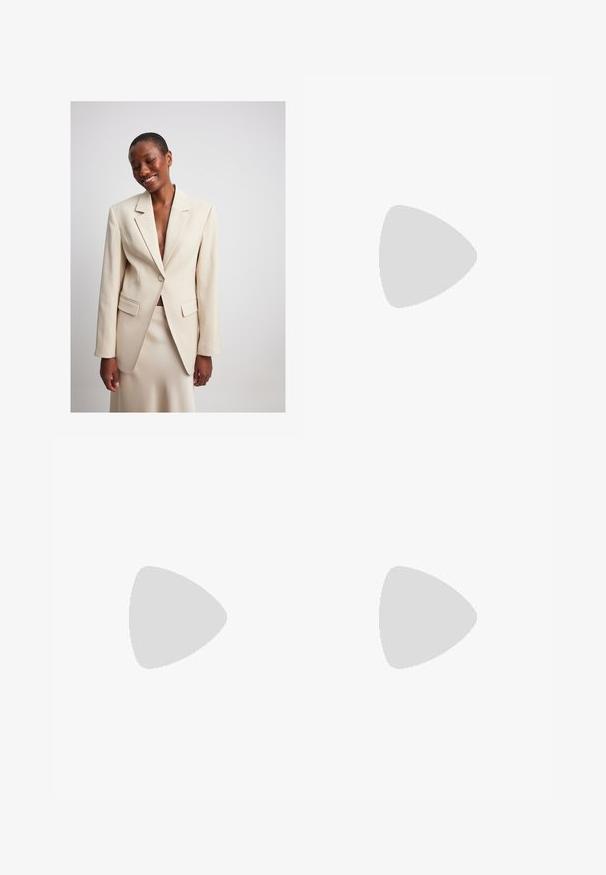 NA-KD Blazer - champagne; Kaotiko CREW PUPPIES UNISEX - Poloshirts - beige; Bredde benbukser i lyse beige stof med en glat tekstur. Har en tætsiddende talje, forkantfolder og ingen synlige lommer.; Brune ruskind sneakers med hvide detaljer og snørebånd. Gummisål i naturgummi. Båret med hvide sokker med sorte striber. Grøn struktureret gulv.