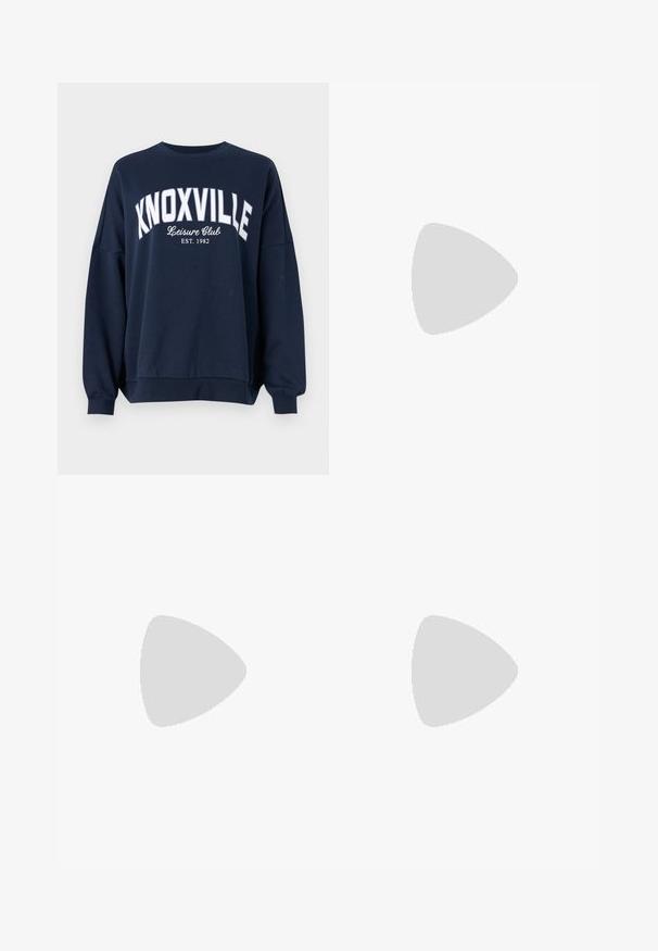 tumši zila džemperis ar baltu tekstu, kas lasāms "KNOXVILLE Atpūtas klubs EST. 1982." Funkcijas: apaļa apkakle un brīvi piegulošas ribotas piedurknes.; Tumšas denima bikses ar šauru piegriezumu, augstu jostasvietu, piecu kabatu dizainu un metāla pogas aizdari. Gluda tekstūra ar nedaudz izbalējušu efektu.; Baltās ādas kedas ar perforētu purngalu, teksturētu zoli un baltām auklām, apvienotas ar platām sarkanām biksēm un zilu un dzeltenu fona.; Sieviete ar garām tumšām matiem, ģērbusies melnā uzvalkā, nēsā melnu ādas plecu somu un skatās pāri plecam uz balta fona.