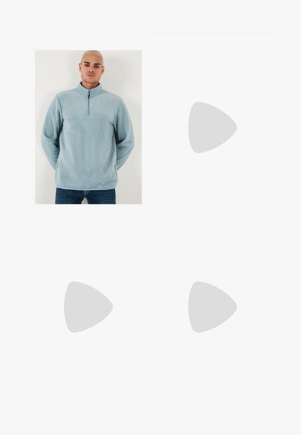 Lichtblauwe fleece pullover met hoge kraag en halve rits aan de voorkant. Zachte textuur met een effen ontwerp en een horizontale naad over de borst.; Wijde blauwe denim jeans met een vervaagde was, vijf zakken en een knoopsluiting. Voorzien van riemlussen en gestikte details.; Bruine sandaal met twee banden en koperen gespen, kurken voetbed en rubberen zool. Strak ontwerp met verstelbare banden voor een goede pasvorm.; Zilveren hanger met een golvende ontwerp dat is verweven met het gezicht van een leeuw, hangend aan een robuuste ketting. Geplateerde oppervlakte voegt detail toe.