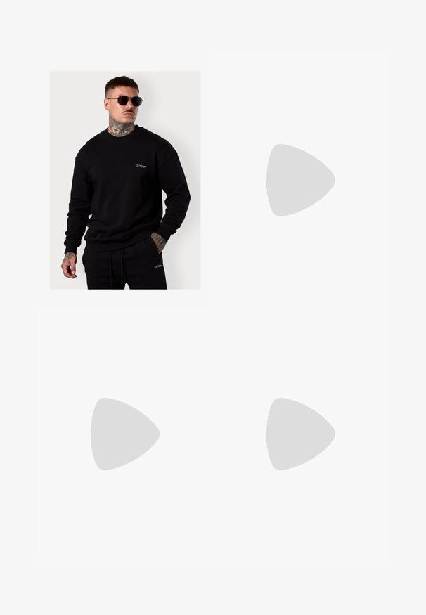 Schwarzer Pullover aus weichem Stoff, mit langen Ärmeln, rundem Ausschnitt und einem kleinen weißen gestickten Logo auf der Brust.; Graue Baumwoll-Loungehosen mit elastischem Bund, Kordelzug und zwei seitlichen Taschen; gerader Schnitt, weiche Textur, ohne Muster.; Beige Wildleder-Ankle-Boot mit schwarzem gepolstertem Kragen, goldenen Metallösen, weißen Nähdetalben und einer robusten Gummisohle mit ausgeprägtem Profil.; Sonnenbrille mit einem schlanken, hellgrauen Kunststoffrahmen, umschließendem Design, dunklen Gläsern und einer glatten Oberfläche. Mit minimaler Markenkennzeichnung an der Seite.