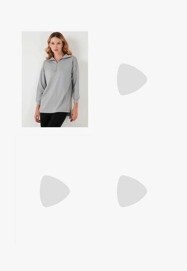 Svetlo sivi pulover s half-zip ovratnikom, dolgimi rokavi in stranskimi razpoki. Gladka tekstura in sproščen kroj.; Črne široke hlače iz gladkega, sijočega materiala z elastičnim pasom in brez vidnih žepov ali kovinskih detajlov.; Črne platnene športne copate z belimi vezalkami, belim gumijastim prstnim zaščitnikom in masivnim belim srednjim podplatom. Imajo subtilne bele šive in gumijast podplat.; Črne pravokotne sončna očala s temnimi lečami in debelimi mat okvirji. Ročaji so rahlo ukrivljeni in imajo gladko teksturo.