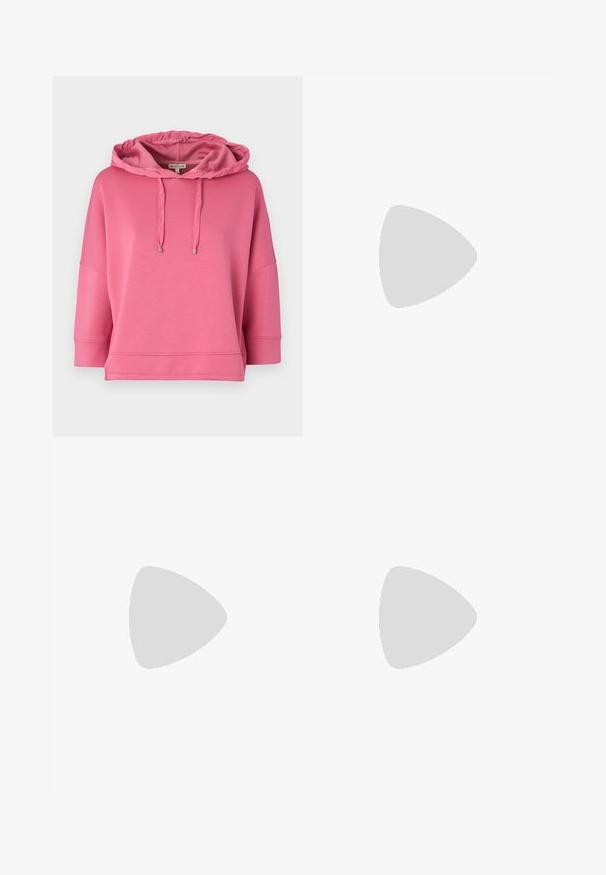 Sweatshirt à capuche rose fabriqué en tissu doux. Dispose d'une coupe décontractée, de manches larges et de cordons avec embouts métalliques.; Pantalon large noir avec un motif floral crème. Fabriqué en tissu léger, il présente une texture lisse et une taille haute.; Baskets de sport noires avec une tige en maille texturée, dotées d'une semelle intermédiaire couleur cuivre, d'une semelle rembourrée et de lacets pour un maintien sûr.; Sac à main noir à la forme structurée, texture lisse et fermoir métallique. Associé à un pantalon noir ample et des sandales ouvertes sur un sol en bois.
