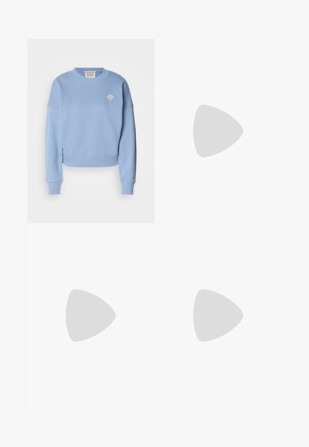 Sweatshirt court bleu clair en matériau doux. Doté d'un col rond, de épaules tombantes et d'un petit motif brodé sur la poitrine.; Pantalons en lin bleu clair avec une coupe droite, fermeture à bouton et ourlet retroussé. Texture lisse, conçus pour un port décontracté.; Baskets basses blanches avec une texture lisse, présentant un accent en daim beige clair sur le talon et une épaisse semelle en caoutchouc blanche.; Lunettes en acétate transparent en forme de yeux de chat avec des verres jaunes, portées par une personne en veste en cuir noir et en col roulé rouge. Texture lisse.