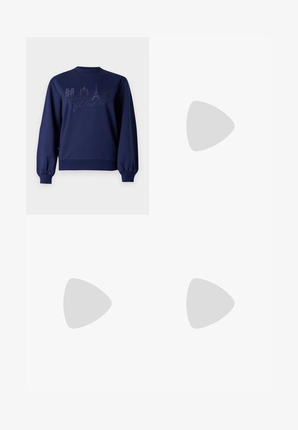 Sweatshirt azul-marinho com decote arredondado, punhos canelados e um bordado do skyline de Paris com texto e pontos de referência notáveis.; Calças largas pretas com um padrão floral creme. Feitas de um tecido leve, apresentando uma textura suave e uma cintura alta.; Sapatilha branca com um cabedal sintético liso, caixa dos dedos perfurada, atacadores planos e uma sola texturizada, exposta sobre uma superfície de madeira.; Bolsa preta com forma estruturada, textura suave e um fecho metálico. Combinada com calças largas pretas e sandálias de salto aberto sobre um chão de madeira.