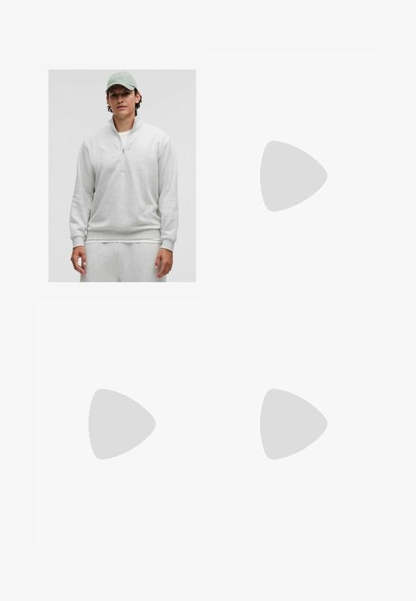 Hellgrauer Reißverschluss-Pullover mit langen Ärmeln, weichem Material und gerippten Bündchen. Wird über einem weißen Shirt getragen und mit passenden Hosen kombiniert.; Olivgrüne Hosen mit taillierter Passform, mit Falten an der Vorderseite, Knopfverschluss und geraden Beinen. Glatte Stofftextur.; Schwarzer Lederloafer mit strukturiertem schwarzen Lederakzent, abgerundeter Zehenform und niedrigem Blockabsatz; verfügt über ein dekoratives metallisches Detail.; Schwarze Plastiksonnenbrille mit grünen Gläsern, quadratischen Rahmen, silbernem Akzent auf der Augenbraue und strukturierten Bügeln. Angegebene Marke auf dem inneren Bügel.