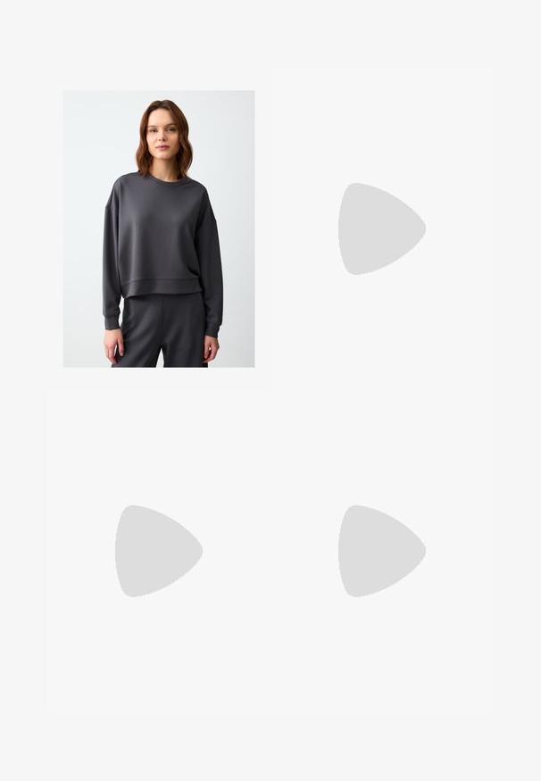 Dark gray sweatshirt with a loose fit, crew neckline, and long sleeves. Made from soft, smooth fabric with a slightly cropped hem.; Black wide-leg trousers with high waist, button details on waistband, and front pleats.; Black leather loafers with a flat heel, featuring a decorative gold hardware detail on the front and a smooth texture.; Black handbag with structured shape, smooth texture, and a metallic clasp. Paired with wide black pants and open-toe sandals on wooden floor.