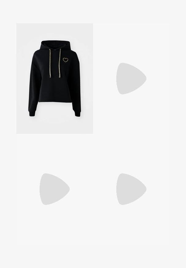 Melna kropta kapuce ar priekšējo kabatu, ar zelta sirds izšuvumu un mirdzošām zelta auklām. Izgatavota no mīksta, teksturēta auduma.; Pelēki plati bikses no denima ar gludu tekstūru, ar pogu un rāvējslēdzēju, kā arī piecām kabatām.; Melnas zamšādas sporta kurpes ar baltām svītrām un akcentiem, apaļa purngala daļa, gumijas zole, kopā ar baltām ribotām sporta zeķēm.; Sieviete ar garām tumšām matiem, ģērbusies melnā uzvalkā, nēsā melnu ādas plecu somu un skatās pāri plecam uz balta fona.