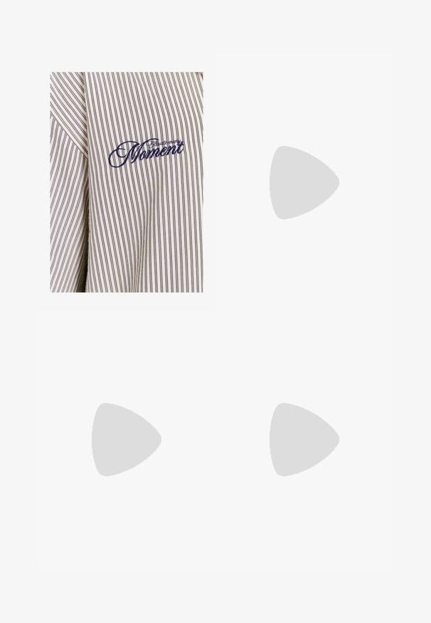 Camisa a rayas en beige claro con líneas verticales en azul oscuro. Presenta un texto bordado que dice "Captura Cada Momento" en hilo azul oscuro.; Camiseta de algodón blanca con mangas cortas y cuello redondo. Presenta un logo negro de "Carhartt" impreso en la parte superior izquierda del pecho.; Pantalones cargo de algodón blancos con un corte relajado. Las características incluyen bolsillos frontales, detalles en dorado y secciones de rodilla reforzadas.; Zapatillas deportivas blancas con superposiciones texturizadas, una suela gruesa y acentos grises. Llevadas con calcetines blancos hasta la pantorrilla y pantalones cortos verdes sobre una superficie azul.