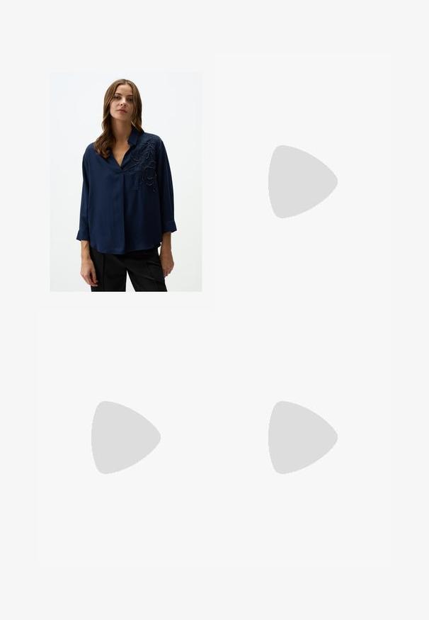 Navy blue blouse with a V-neck, 3/4 sleeves, and intricate black floral embroidery on the left side. Smooth fabric with subtle sheen.; Denim wide-leg jeans with a medium blue wash, two front pockets with button closures, and stitched detailing along the hems.; White leather sneakers with smooth texture, padded ankle, and perforated toe. Features a slightly elevated rubber sole and lace-up design.; Brown leather tote bag with a smooth texture, open top design, and two shoulder straps. Features minimal stitching and no visible hardware.