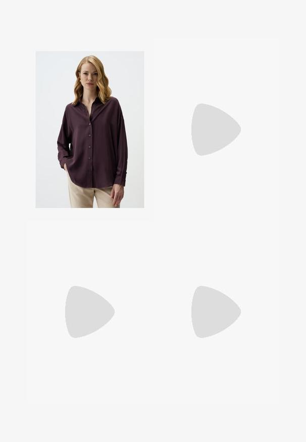 Donkerpaarse blouse met een relaxte pasvorm, lange mouwen en een kraag. Glad textuur met een subtiele glans, gecombineerd met lichtgekleurde broeken.; Zwarte wijde broek met hoge taille, knoopdetails op de tailleband en plooien aan de voorkant.; Zwarte leren pump met een spitse neus en een lage blokhak. Beschikt over een enkelband met een goudkleurige gespsluiting. Gladde textuur.; Zwarte handtas met gestructureerde vorm, gladde textuur en een metalen sluiting. Gecombineerd met brede zwarte broeken en sandalen met open teen op een houten vloer.