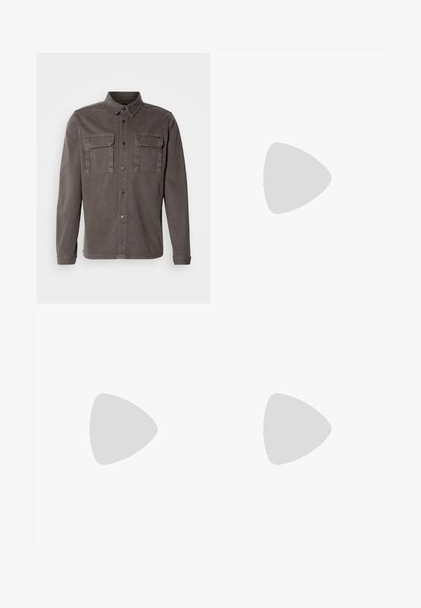 Sivá košeľová bunda z bavlnenej zmesi s dvoma náprsnými vreckami, gombíkovým zapínaním a point collar; má dlhé rukávy a rovný lem.; Krémové bavlnené tričko s krátkymi rukávmi, na ktorom je zelená grafika s kempingovou tematikou a text "PHOENIX 112.0740".; Tmavomodré denimové džínsy s úzkym strihom, obsahujúce päť vreciek, predné zapínanie na gombík a jemne vyblednutú textúru na nohách.; Biele tenisky s hladkým povrchom, s hnedými koženými akcentmi a čiernymi detailmi, spárované s čiernymi elegantnými nohavicami. Pozadím je drevená podlaha.