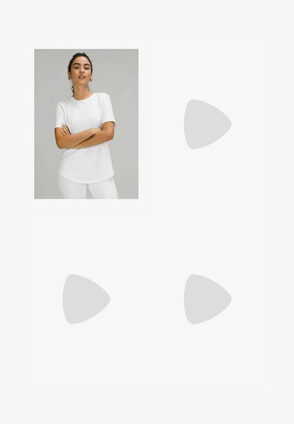 Bela kratka majica s kratkimi rokavi iz gladkega materiala, z okroglo izrezom in zaobljenim robom. Nosijo jo z belimi hlačami.; Sive legice z gladkim, raztegljivim materialom, visokim pasom in oprijetim krojem, zasnovane za udobje in prosto gibanje.; Bela športna obutev z teksturiranim zgornjim delom, črtastimi poudarki in oblazinjenjem podplata. Opremljena je z vezalkami in zaobljenim dizajnom toe.; Črna torba za rame z mehkobo teksturo, z dvema kratkima ročajema in stranskim žepom, ki je zavarovan z vrvico. Preprost, angularen dizajn.