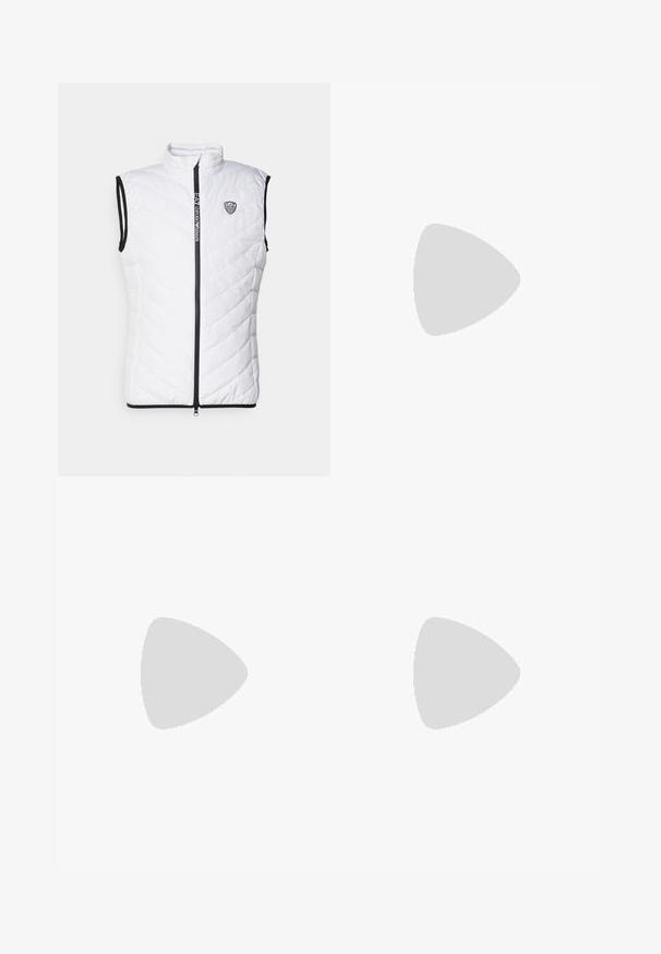 Bijela bezrukavna puffer prsluk s visokim vratom, dijamantnim štepom, crnim patent zatvaračem i suptilnim logom na prsima.; Tamno plava pamučna majica s horizontalnom plavom prugom i tamnosivim donjim dijelom. Sadrži mali logo na gornjem lijevom dijelu.; Bež hlače ravnog kroja, s pojasom na vezivanje, nabranim prednjim dijelom i glatkom teksturom. Jednostavan, svestran dizajn.; Crne nubuk tenisice s bijelim gumenim potplatima, s zaobljenim vrhom i vezicama, uparene s sivim krojenim hlačama.