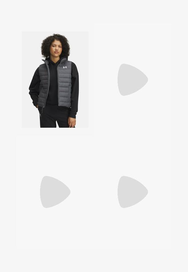 Usztywniona szara kamizelka z zamkiem błyskawicznym z przodu i wysokim kołnierzem, noszona na czarnej bluzie z kapturem. Posiada poziome przeszycia i logo Under Armour na klatce piersiowej.; Czarna, długosleeve'owa koszulka sportowa z gładkiego materiału, z okrągłym dekoltem i małym białym logo na lewej piersi.; Czarne legginsy wykonane z gładkiego, elastycznego materiału z wysokim stanem. Posiadają białe logo na lewym udzie oraz dopasowany krój.; Czarne buty sportowe z teksturowanym materiałem, białą podeszwą i czarnymi sznurowadłami. Nosi je osoba w białych skarpetkach w prążki, stojąca na jasnej powierzchni.